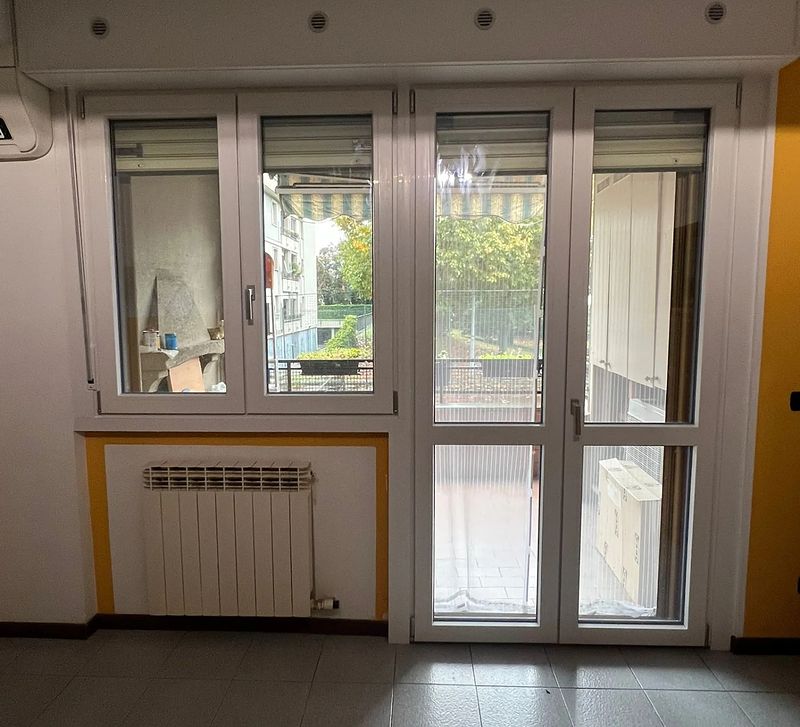 Finestra e porta-finestra in PVC bianco con tapparelle, in un soggiorno.